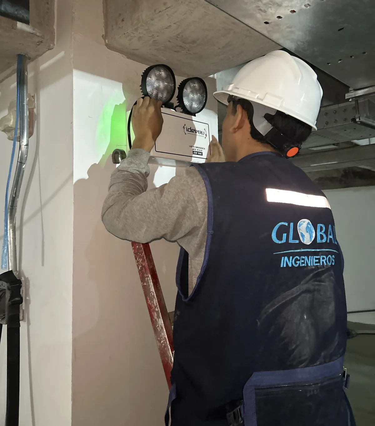 Técnico de Global Ingenieros instalando una luz de emergencia de dos focos en un local