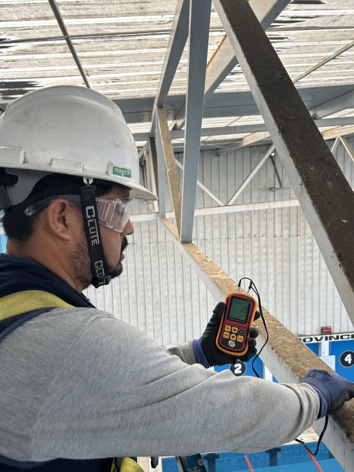 Ingeniero de Global Ingenieros con casco, lentes y arnés midiendo el espesor de una viga metálica con un medidor por ultrasonido