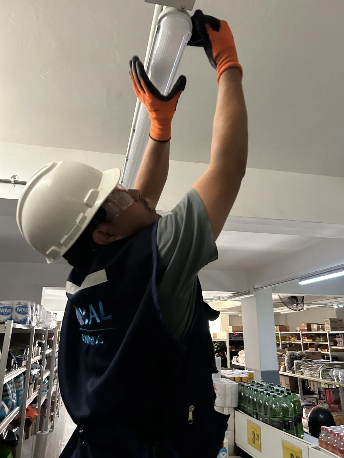 Técnico con casco y guantes revisando una luminaria de emergencia en el techo de una tienda