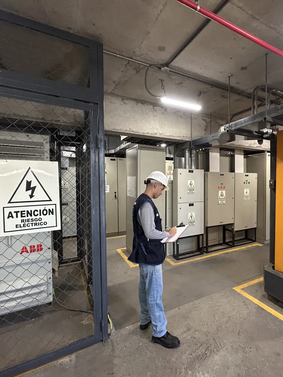 Ingeniero anotando en la sala de tableros eléctricos y grupo electrógeno, junto a la señal de riesgo eléctrico